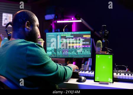 Tontechniker komponieren neue Melodien mit daw-Schnittstelle, die auf dem Greenscreen-Display arbeitet. afroamerikanischer Musiker, der seine Aufnahmen, Stereo-Konsole und Ausrüstung mischt und meistert. Stockfoto