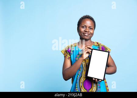 Selbstbewusste Frau, die ein Tablet mit leerem Mockup-Layout zeigt und Werbung mit isolierter Copyspace-Vorlage auf einem drahtlosen Gerät erstellt. Das afroamerikanische Mädchen präsentiert ein weißes Display vor der Kamera. Stockfoto