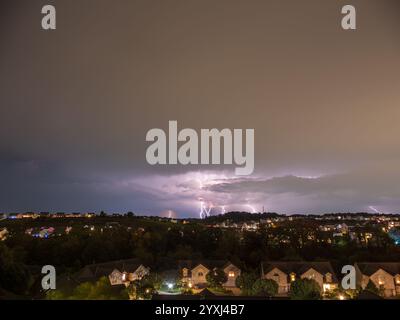 Dunkle Gewitterwolken erheben sich über einem amerikanischen Viertel, in dem der Himmel in einem aufregenden Schauspiel der Kraft der Natur erleuchtet wird. Stockfoto