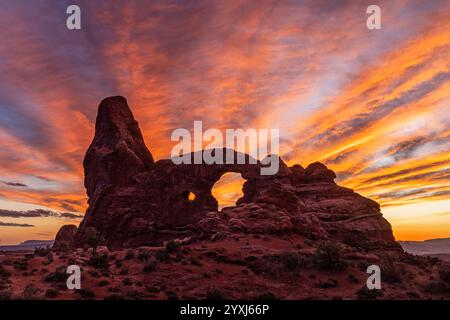 Die vom Wind verwobenen Wolken leuchten bei Sonnenuntergang über dem Turret Arch im Windows Section des Arches National Park in Moab, Utah, auf spektakuläre Weise auf. Stockfoto