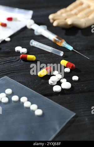 Drogensucht. Plastiktüte mit Pillen und Spritze auf schwarzem Holztisch, Nahaufnahme Stockfoto