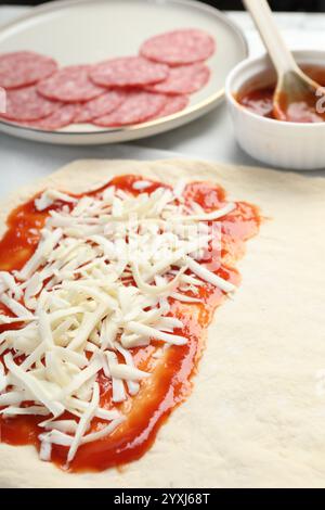 Zubereitung von Calzone-Pizza. Teig mit Sauce, Käse und anderen Zutaten auf dem Tisch, Nahaufnahme Stockfoto