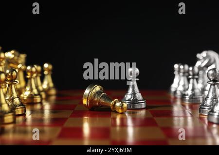 Silberner Bauer in der Nähe von gefallenem goldenem und anderen Schachfiguren auf Schachbrett vor schwarzem Hintergrund, Nahaufnahme. Wettbewerbskonzept Stockfoto