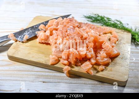 Roher Lachs, in kleine Würfel geschnitten für Tartar oder Ceviche auf einem hölzernen Küchenbrett mit Messer und Dill, Zubereitung für ein köstliches Fischgericht, ausgewählt Stockfoto