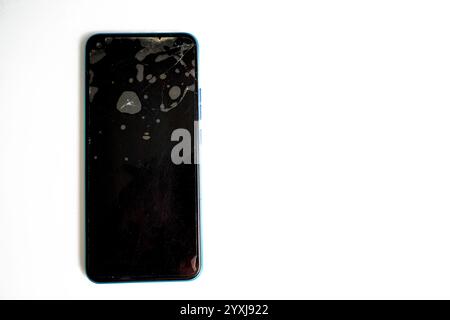 Ein Smartphone mit sichtbar gerissenem Bildschirm und Flecken liegt auf einer sauberen weißen Oberfläche. Der Bildschirm des Geräts zeigt Anzeichen von Beschädigungen an, die auf eine vorherige Verwendung hinweisen Stockfoto