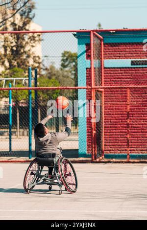 Junger Latino-Athlet im Rollstuhl, Training, Basketball spielen und schießen in einem Stadtpark im Freien Stockfoto