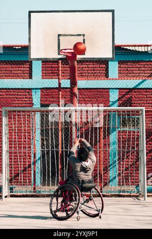 Junger Latino-Athlet im Rollstuhl, Training, Basketball spielen und schießen in einem Stadtpark im Freien Stockfoto