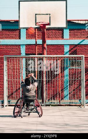 Junger Latino-Athlet im Rollstuhl, Training, Basketball spielen und schießen in einem Stadtpark im Freien Stockfoto