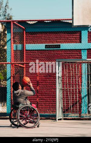 Junger Latino-Athlet im Rollstuhl, Training, Basketball spielen und schießen in einem Stadtpark im Freien Stockfoto