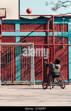 Junger Latino-Athlet im Rollstuhl, Training, Basketball spielen und schießen in einem Stadtpark im Freien Stockfoto