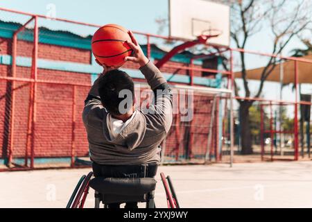 Junger Latino-Athlet im Rollstuhl, Training, Basketball spielen und schießen in einem Stadtpark im Freien Stockfoto