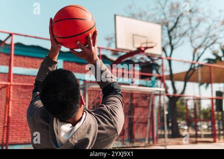 Junger Latino-Athlet im Rollstuhl, Training, Basketball spielen und schießen in einem Stadtpark im Freien Stockfoto