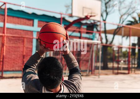 Junger Latino-Athlet im Rollstuhl, Training, Basketball spielen und schießen in einem Stadtpark im Freien Stockfoto