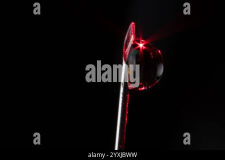 Makrophotographie eines Wassertropfens, der an der Spitze der Spritzennadel befestigt ist. Mit rotem Licht, das auf den Wassertropfen leuchtet Stockfoto