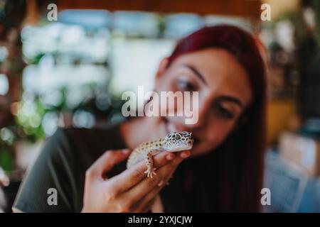 Junge Frau, die fröhlich mit einer freundlichen Eidechse in einer lebendigen Innenumgebung spielt und eine einzigartige Verbindung mit der Natur zeigt Stockfoto