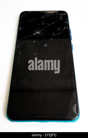 Ein beschädigtes Smartphone liegt auf einer weißen Oberfläche auf und zeigt einen gerissenen Bildschirm mit Flecken. Das Gerät weist darauf hin, dass eine Reparatur oder ein Austausch erforderlich ist Stockfoto