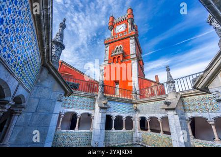 Ein lebendiger Innenhof mit komplizierten Fliesenmustern und einem markanten roten Uhrenturm. Weitere Details sind Steinsäulen und dekorative Elemente, Pen Stockfoto