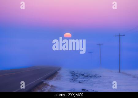 Die untergehende Sonne fällt in eine Nebelbank am Highway 561 in Alberta, Kanada. Stockfoto