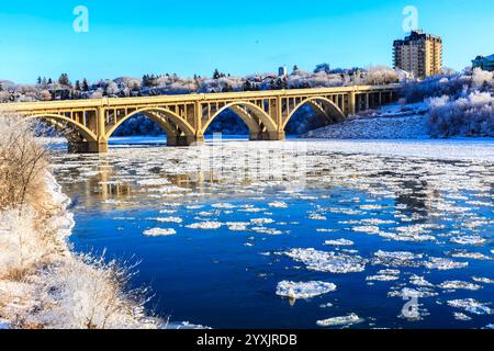 Eine Brücke über einen Fluss mit Eis auf dem Wasser. Die Brücke ist groß und erstreckt sich über den Fluss. Das Wasser ist gefroren und die Brücke ist von Bäumen umgeben Stockfoto