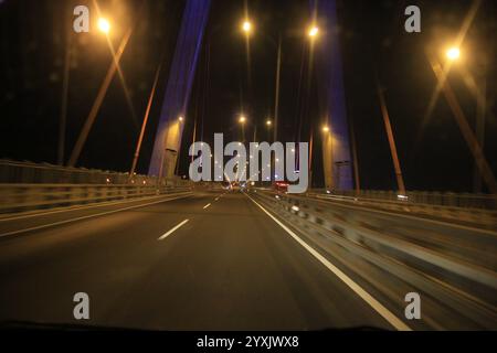 Verschwommenes Bild, Blickwinkel des Fahrers, der sein Fahrzeug nachts über eine Brücke fährt Stockfoto