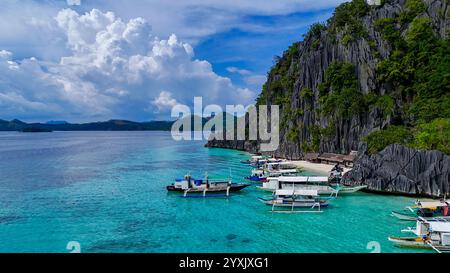 Eine atemberaubende tropische Szene mit klarem türkisfarbenem Wasser, traditionellen Holzbooten und dramatischen Kalksteinklippen, die mit üppigem Grün bedeckt sind. Sm Stockfoto