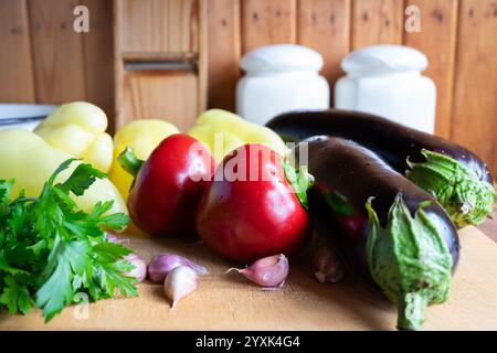 Eine Vielzahl von frischem Gemüse, einschließlich Paprika, Auberginen und Knoblauch, ist auf einem Schneidebrett in einer warmen, rustikalen Küche, Showcasin, ordentlich angeordnet Stockfoto