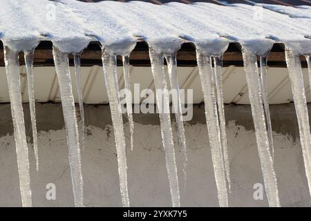 Scharfe Eiszapfen und geschmolzener Schnee hängen von Dachtrassen. Wunderschöne, transparente Eiszapfen, die langsam über ein Dach gleiten. Stockfoto