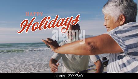 Bild des weihnachtsgrüßtextes über ein vielseitiges Seniorenpaar, das Selfie am Strand macht. Weihnachten, Tradition, Feier und Festtagskonzept digital Stockfoto