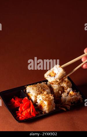 Essstäbchen nehmen eine Portion Sushi-Rolle. Sushi-Brötchen mit Lachs-Frischkäse und Gurke zum Mitnehmen. Konzept für die Lieferung von Lebensmitteln. Stockfoto