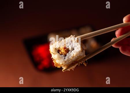 Essstäbchen nehmen eine Portion Sushi-Rolle. Sushi-Brötchen mit Lachs-Frischkäse und Gurke zum Mitnehmen. Konzept für die Lieferung von Lebensmitteln. Stockfoto