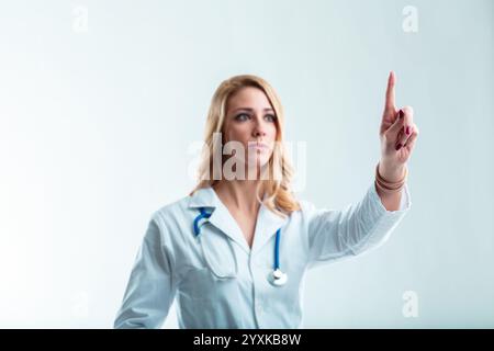 Verschwommene Ärztin, blond im weißen Mantel, Gesten, um deine schwebende Grafik zu platzieren. Ein Wissenschaftler im High-Tech-Krankenhaus-Setting Stockfoto
