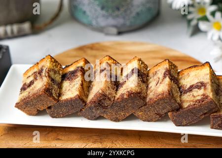 Hausgemachte Marmor-Kuchen-Quadrate auf einem Holztablett mit Tee-Setup-Blumen-Hintergrund Stockfoto