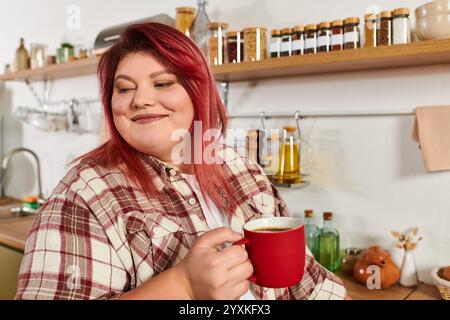 Eine junge Frau mit lebhaften Haaren schlürft Kaffee in einer wunderschön eingerichteten Küche, die mit Gläsern gefüllt ist. Stockfoto