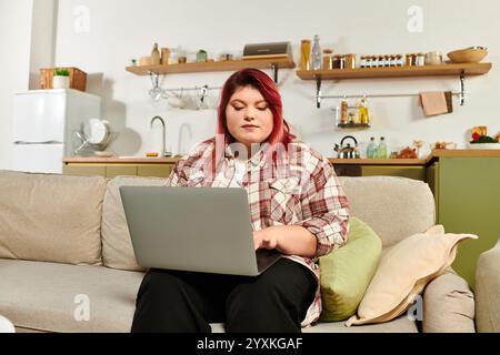 Junge Frau in Übergröße konzentrierte sich auf ihren Laptop, während sie sich in einem warmen und einladenden Wohnbereich entspannte. Stockfoto