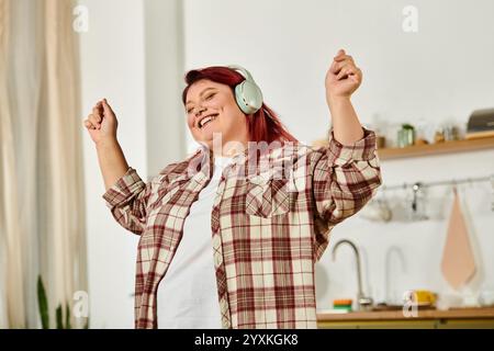 Eine junge Frau mit roten Haaren tanzt glücklich in ihrer gemütlichen Küche, während sie Musik hört. Stockfoto