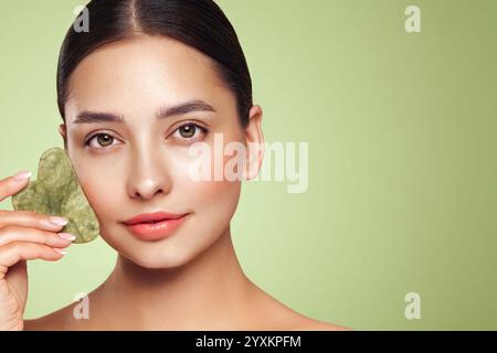 Schönheit junge Frau, die Hautpflegeroutine macht, abkratzt, Gesichtshaut mit Jade Gua Sha Scrapper massiert, Gesichtsbehandlung für Anti-Aging und Kosmetik cl Stockfoto