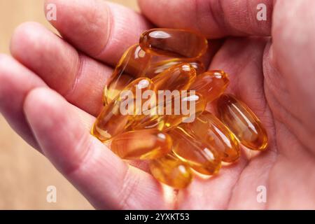 Omega-3-Kapseln mit EPA und DHA in einer Hand. Goldene, durchscheinende Softgels aus nächster Nähe Stockfoto