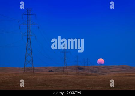 Vollmond, der am Ende einer langen Reihe von Hochspannungstürmen in Alberta, Kanada, aufsteigt. Stockfoto