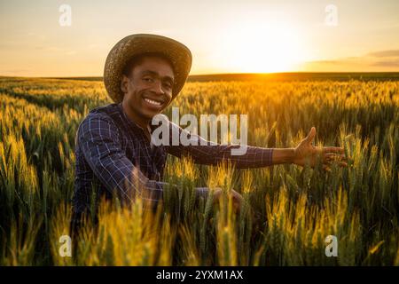 Porträt eines afrikanischen Bauern auf seinem wachsenden Weizenfeld. Er ist zufrieden mit dem Fortschritt der Pflanzen. Erfolgreicher Landwirt in der Landwirtschaft. Stockfoto