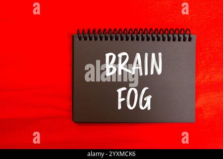 Gehirnnebel-Nachricht auf schwarzer Notizbuchseite mit rotem Hintergrund. Konzeptionelles Hirnnebelsymbol. Kopierbereich. Stockfoto