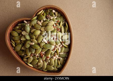 Kürbis-, Flachs- und Sonnenblumenkerne in einer herzförmigen Holzschale. Stockfoto