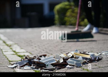 Eine Person fegt zerbrochenes Glas auf einem Bürgersteig auf. Die Szene ist chaotisch und unorganisiert, mit zerbrochenen Glasstücken, die über den Boden verstreut sind. Th Stockfoto