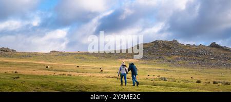 Ein Panoramablick von Tywo-Leuten, die auf den imposanten Granitgrat Roughtor Rough Tor auf dem wilden windgepeitschten Bodmin Moor in Cornwall in gehen Stockfoto