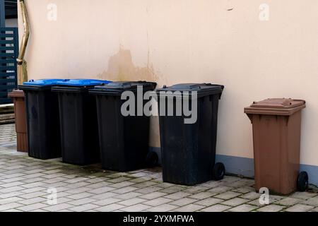 Verschiedene Mülleimer in verschiedenen Farben sind an einer Gebäudewand angeordnet. Der Bereich scheint gut gepflegt und zeigt eine saubere und organisierte Umgebung. Stockfoto