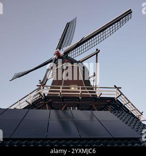 Eine niederländische Windmühle kombiniert mit Solarpaneelen auf einem Fliesendach, symbolisiert die lange Tradition erneuerbarer Energien und Nachhaltigkeit in den Niederlanden. Stockfoto