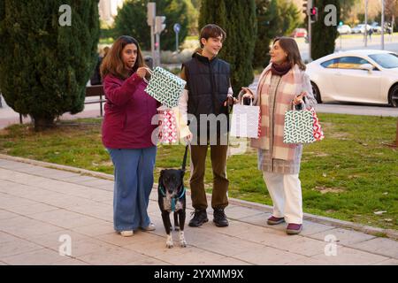 Fröhliche Familie, die die Weihnachtszeit feiert und nach dem Einkaufen in der Stadt weihnachtsgeschenke präsentiert und die Zeit mit ihrem Hund an der Leine genießt Stockfoto