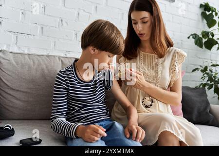 Eine junge Mutter hilft ihrem Sohn, seinen Diabetes zu Hause in ihrem gemütlichen Wohnzimmer zu überwachen. Stockfoto