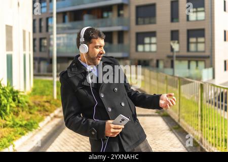 Erwachsener kaukasischer Geschäftsmann in lässiger Winterkleidung tanzt während er Musik mit Handy und Kopfhörern in der Stadt hört Stockfoto