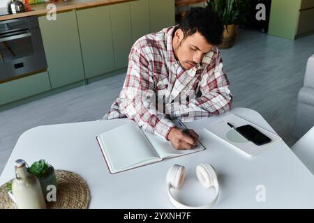 Der hübsche junge Mann schreibt Notizen in einem Notizbuch an einem stilvollen Küchentisch. Stockfoto