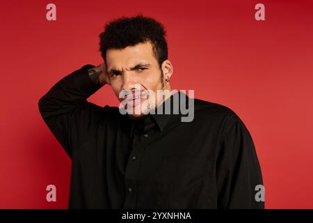 Ein hübscher junger Mann steht mit einer Hand am Hals und zeigt einen neugierigen Ausdruck. Stockfoto